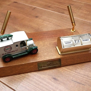 May include: A wooden desk organizer featuring a miniature white and green Heinz delivery truck model, a gold-toned perpetual calendar displaying Tuesday 25 December, and two gold pen holders. A brass plaque on the front reads Heinz Centennial.