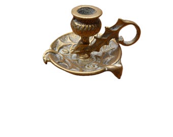 May include: A vintage brass candlestick holder with a decorative leaf design. The candle holder has a round base with a handle and a cup for a single candle. The brass has a warm, aged patina.