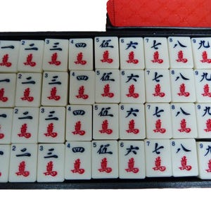 Peut inclure: Un plateau noir contenant trente-six tuiles de mah-jong blanches dispos&eacute;es en quatre rang&eacute;es. Chaque tuile pr&eacute;sente un chiffre noir de un &agrave; neuf en haut et un caract&egrave;re chinois rouge pour dix mille en bas, avec quatre exemplaires par chiffre.