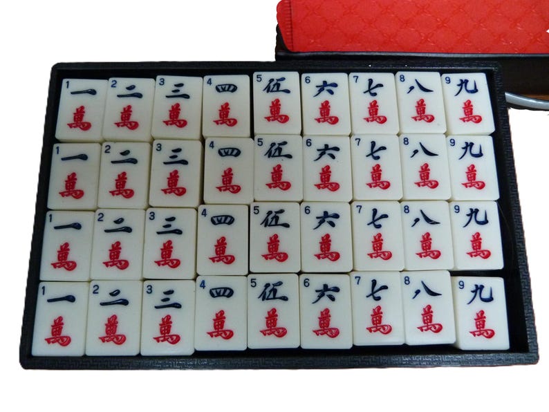 Peut inclure: Un plateau noir contenant trente-six tuiles de mah-jong blanches dispos&eacute;es en quatre rang&eacute;es. Chaque tuile pr&eacute;sente un chiffre noir de un &agrave; neuf en haut et un caract&egrave;re chinois rouge pour dix mille en bas, avec quatre exemplaires par chiffre.