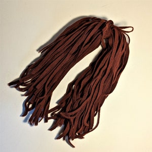 May include: A bundle of dark brown shoelaces, arranged in a loose, flowing pattern. The laces are made of a woven material and have a slightly frayed appearance at the ends. The color is a rich, earthy tone, suitable for various shoe styles.
