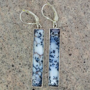 May include: A pair of drop earrings featuring rectangular dendritic agate stones with white backgrounds and black fern-like inclusions, set in silver-toned metal frames with lever-back closures for secure attachment to the earlobes.
