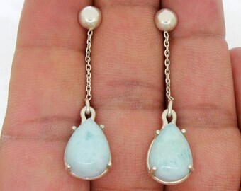 May include: A pair of silver dangle earrings with light blue teardrop-shaped stones. The stones have a cloudy, marbled appearance.