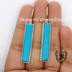 May include: A pair of silver dangle earrings with turquoise blue rectangular stones. The earrings are approximately 5 cm long.
