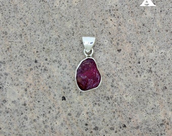 May include: A silver pendant featuring a raw, red ruby gemstone. The ruby is irregularly shaped and has a natural, rough texture.