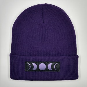 May include: Purple knitted beanie with a black patch featuring a moon phase design.