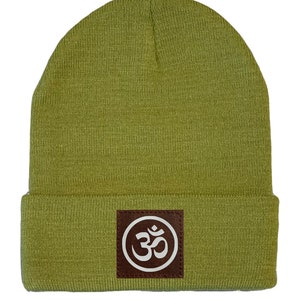 May include: A green beanie with a brown leather patch featuring a white Om symbol.