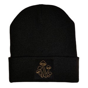 Puede incluir: Gorro negro con un contorno dorado de setas bordadas en la parte delantera.