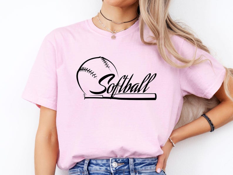 K&ouml;nnte beinhalten: Ein hellrosa T-Shirt mit kurzen &Auml;rmeln und einem schwarzen Grafikdruck auf der Brust. Das Design zeigt einen Softball und einen Schl&auml;ger, wobei das Wort Softball in einer kursiven Schriftart in der Mitte abgebildet ist.