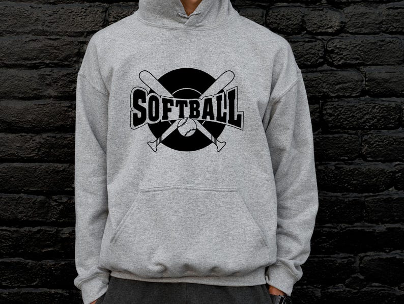 K&ouml;nnte beinhalten: Ein hellgrauer Kapuzenpullover mit einem schwarzen Grafikdruck auf der Brust. Das Design zeigt das Wort SOFTBALL in fetten Gro&szlig;buchstaben, &uuml;berlagert von zwei gekreuzten Baseballschl&auml;gern und einem Softball in einem soliden schwarzen Kreis.