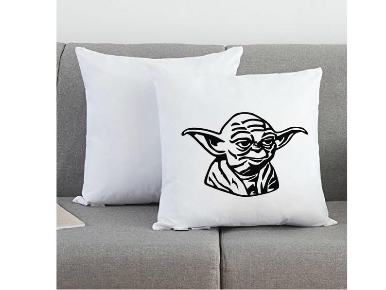 May include: Two square white throw pillows. One pillow is plain white, while the other features a bold, black graphic illustration of the character Yoda, showing the head and shoulders with pointed ears and facial wrinkles in a stylized design.