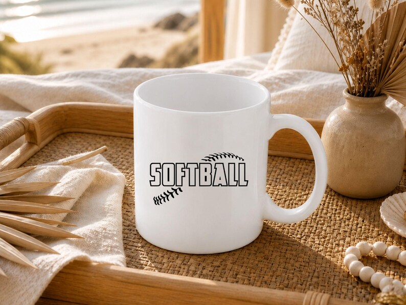 K&ouml;nnte beinhalten: Ein wei&szlig;er Keramikbecher mit einer schwarzen Grafik eines Softballs und dem Wort SOFTBALL, das in fetten, blockartigen Gro&szlig;buchstaben in der Mitte aufgedruckt ist. Der Becher hat einen glatten, zylindrischen K&ouml;rper und einen geschwungenen Henkel.