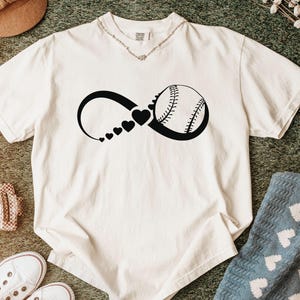 K&ouml;nnte beinhalten: Ein cremefarbenes Kurzarm-T-Shirt mit einem schwarzen Grafikdruck eines Unendlichkeitssymbols. Das Symbol enth&auml;lt eine Reihe kleiner Herzen, die an Gr&ouml;&szlig;e zunehmen und in eine Baseball-Illustration auf der rechten Seite &uuml;bergehen.
