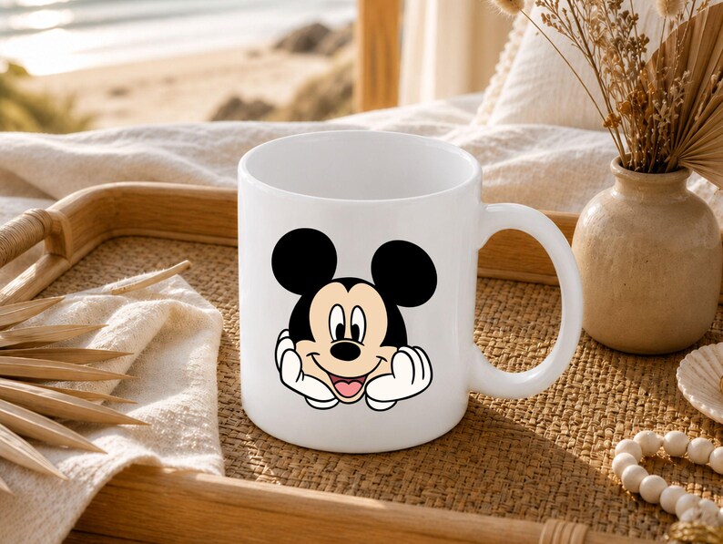 Pu&ograve; includere: Una tazza in ceramica bianca con un'illustrazione grafica di Topolino che appoggia il mento sulle mani. Il personaggio ha orecchie nere, un viso color carne e un ampio sorriso. La tazza ha un corpo cilindrico liscio con un manico curvo laterale.