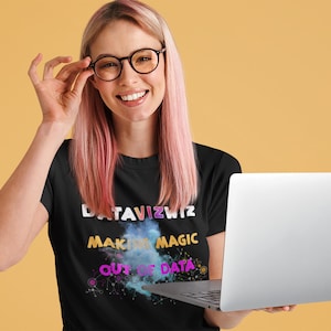 Puede incluir: Una mujer con el pelo rosa lleva una camiseta negra con el texto "DATAVIZWIZ MAKING MAGIC OUT OF DATA" en letras de colores. Está sosteniendo un portátil plateado frente a ella.