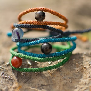 May include: A stack of colorful bracelets with different colored beads, including black, orange, green, blue, and red.