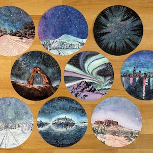 Puede incluir: Una colección de nueve pinturas circulares en acuarela que representan diversas escenas nocturnas. La obra de arte incluye paisajes como montañas nevadas, un horizonte urbano y la aurora boreal, todo bajo cielos estrellados. Cada pieza es un paisaje único y detallado.