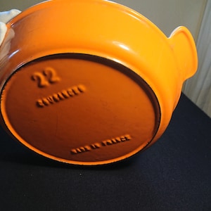 Può includere: Piatto da forno in ghisa smaltata arancione con due manici. Il fondo del piatto è contrassegnato con "22" e "MADE IN FRANCE".