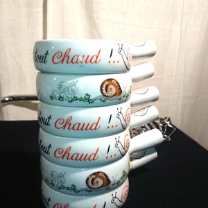 May include: A stack of five white ceramic bowls with a snail design and the text "Tout Chaud!" in red and black. The bowls are designed for serving fondue.