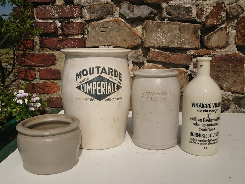 Puede incluir: Colecci&oacute;n de tarros y botellas de cer&aacute;mica antiguos. El tarro m&aacute;s grande es blanquecino con el texto "MOUTARDE IMPERIALE". Un tarro m&aacute;s peque&ntilde;o tiene "AVANNESS LIEGL". Una botella dice "VINAIGRE VIEUX de vin rouge".