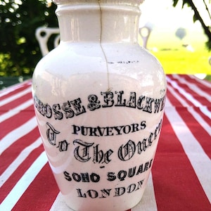 May include: A white ceramic jar with a cork lid. The jar has black lettering that reads " Crosse & Blackwell Purveyors To The Queen Soho Square London ".