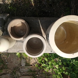 Puede incluir: Vista a&eacute;rea de varias piezas de cer&aacute;mica de gres antiguas. La colecci&oacute;n incluye una botella, dos macetas peque&ntilde;as y un cuenco grande. Las piezas son de varios tonos beige y marr&oacute;n, con un aspecto envejecido. Los art&iacute;culos est&aacute;n colocados sobre una superficie de hormig&oacute;n.
