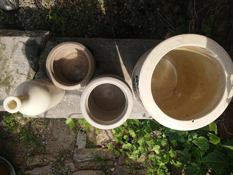 Puede incluir: Vista a&eacute;rea de varias piezas de cer&aacute;mica de gres antiguas. La colecci&oacute;n incluye una botella, dos macetas peque&ntilde;as y un cuenco grande. Las piezas son de varios tonos beige y marr&oacute;n, con un aspecto envejecido. Los art&iacute;culos est&aacute;n colocados sobre una superficie de hormig&oacute;n.