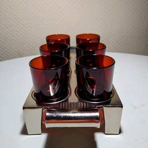 Puede incluir: Un juego de seis vasos de chupito pequeños de color rojo oscuro en una bandeja de plata con asa. Los vasos están dispuestos en dos filas de tres.