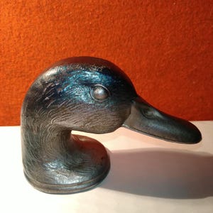 Peut inclure: Une sculpture vintage en métal représentant une tête de canard avec une finition sombre et patinée. La sculpture présente des textures de plumes détaillées et un cou incurvé, avec un bec et un œil proéminents. La tête de canard est probablement un objet décoratif.