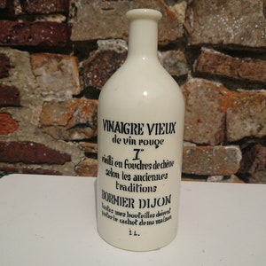 Puede incluir: Botella de cer&aacute;mica blanquecina con texto negro. La botella dice "VINAIGRE VIEUX de vin rouge" y "BORNIER DIJON". La botella tiene un volumen de 1 litro. El fondo es una pared de ladrillos.