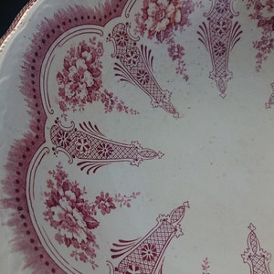 May include: A white plate with a scalloped edge and a burgundy floral and geometric pattern. The plate features a repeating design of flowers and decorative shapes, creating a vintage aesthetic.