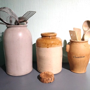 Puede incluir: Tres tarros de cerámica con tapas, dos son blancos con tapas marrones y uno es marrón con tapa blanca. Los tarros están sobre una superficie gris. El tarro de la derecha tiene la palabra "Cornichons" escrita en él.