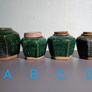 Può includere: Quattro vasi in ceramica verde e blu con coperchi, etichettati A, B, C e D. I vasi sono decorati con motivi floreali e hanno una forma esagonale.