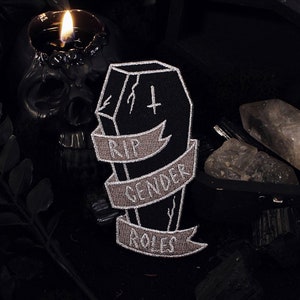 Peut inclure: Un patch brodé noir et blanc avec un cercueil et une bannière qui dit "RIP Gender Roles".