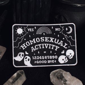 May include: A black and white rectangular patch with the words "HOMOSEXUAL ACTIVITY". The design includes a sun, rainbow, moon, ghosts, skulls, and numbers. The words "YES", "NO", and "GOOD BYE" are also present.