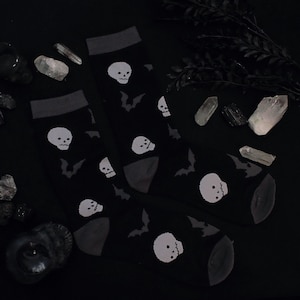 May include: A pair of black socks with a white skull and bat pattern. The socks are on a black background with crystals and other decorative items.