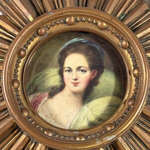 May include: A vintage gold sunburst frame with a miniature portrait of a woman wearing a blue headband. The portrait is painted in watercolour and shows the woman with her hair pulled back and a light green background.