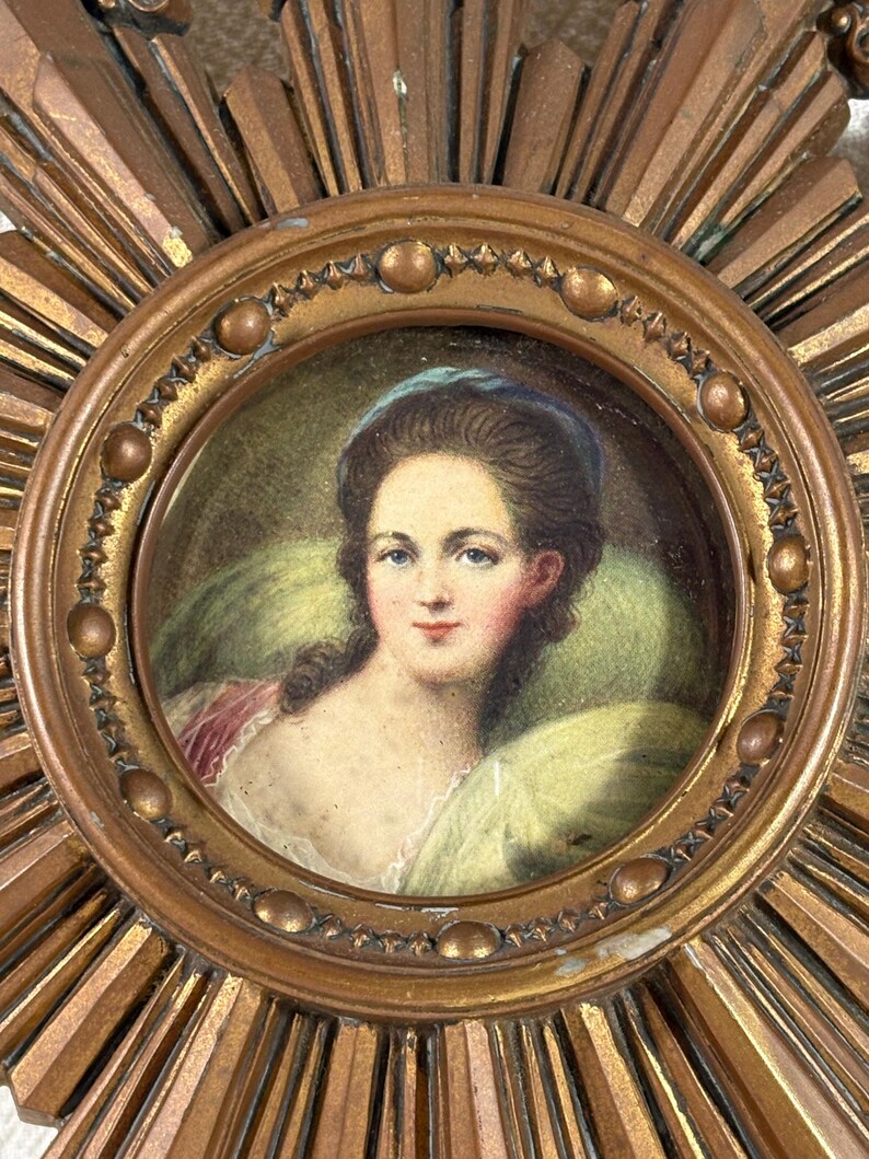 May include: A vintage gold sunburst frame with a miniature portrait of a woman wearing a blue headband. The portrait is painted in watercolour and shows the woman with her hair pulled back and a light green background.