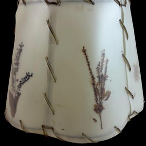 May include: A white lampshade with a scalloped edge and a wire trim. The lampshade has pressed dried flowers and leaves embedded in the fabric.