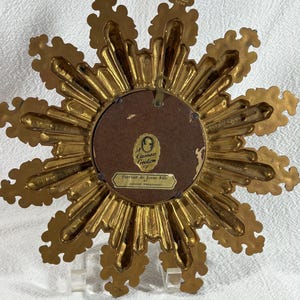 May include: Gold-toned starburst-shaped picture frame with a cameo creation label on the back. The label reads "Cameo Creation" and "Portrait de Jeune Fille par Honore Fragonard".