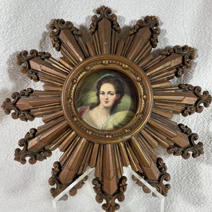 May include: A gold sunburst frame with a miniature portrait of a woman in a green dress. The frame has a decorative design with a raised edge and a beaded border.