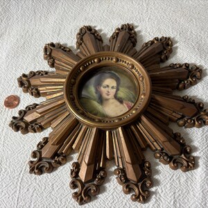 May include: A gold sunburst wall decor with a round portrait of a woman in a white dress and a gold frame.