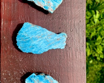 May include: Three blue apatite crystal stones on a brown wooden surface. The stones are different shapes and sizes.
