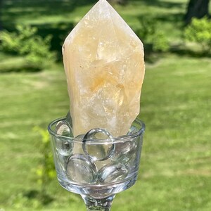 May include: A clear glass candle holder with a yellow crystal point on top. The candle holder is filled with clear glass beads.