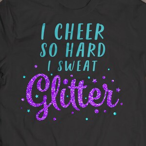 May include: A dark gray t-shirt with the text "I cheer so hard I sweat glitter" in teal and purple glitter lettering.