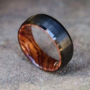 May include: A black and brown wood ring with a brushed finish. The ring is made of tungsten carbide and wood.