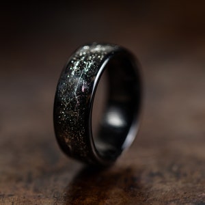 K&ouml;nnte beinhalten: Ein schwarzer Ring mit einem silbernen und wei&szlig;en, gesprenkelten Design. Der Ring ist aus einem strapazierf&auml;higen Material gefertigt und hat eine glatte, polierte Oberfl&auml;che.