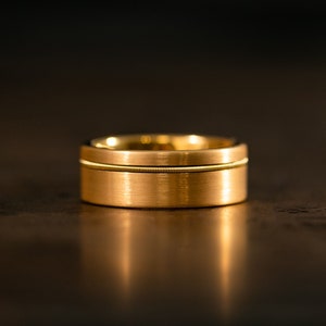 Puede incluir: Una banda de boda de oro con un acabado cepillado y una fina ranura alrededor del centro.