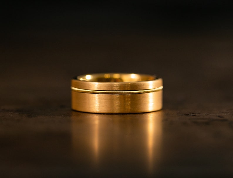 Puede incluir: Una banda de boda de oro con un acabado cepillado y una fina ranura alrededor del centro.