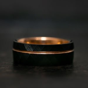 Puede incluir: Un anillo de carburo de tungsteno negro con una banda de oro rosa. El anillo tiene un patr&oacute;n de corte de diamante.